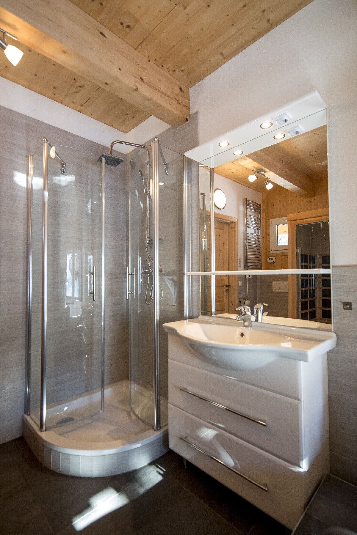 A modern bathroom with a glass-enclosed shower, a white vanity with a large mirror, and wooden ceiling beams.