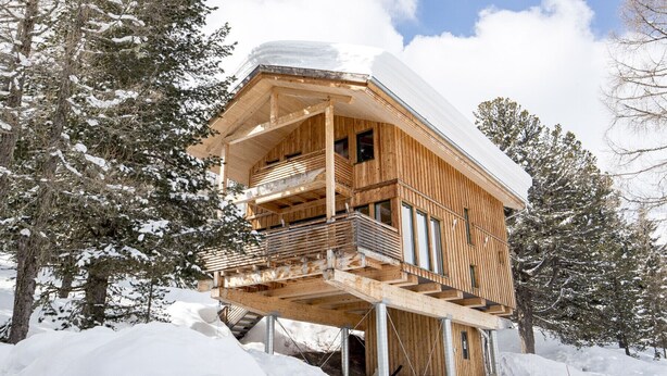Een houten chalet met een balkon, omringd door met sneeuw bedekte bomen.