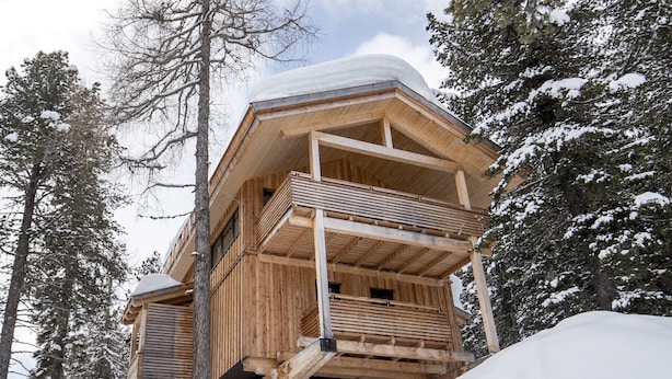 Una baita di legno con un balcone, immersa tra alberi innevati.