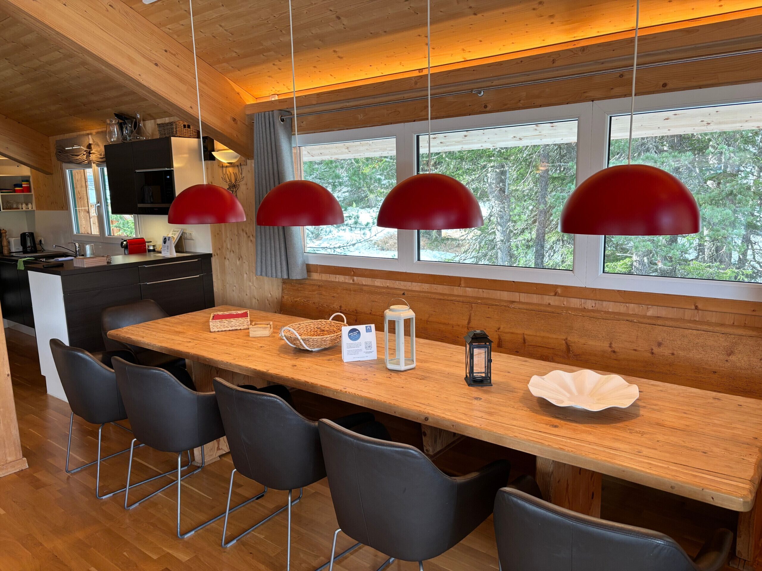 A modern kitchen with a wooden island, black chairs, and red pendant lights.
