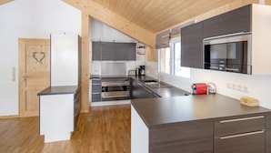 Una cucina moderna con travi in legno, forno a incasso, microonde e macchina per il caffè.