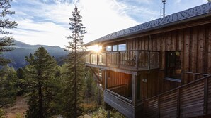 A wooden cabin with a balcony overlooking a forested valley and mountains.