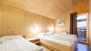 A wooden cabin bedroom with two beds, a small table, and a window with curtains.