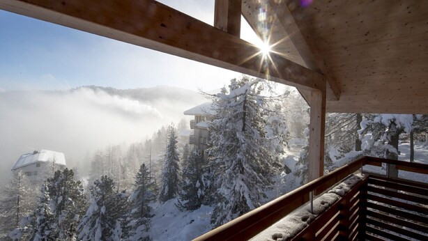 A wooden balcony with a view of a snow-covered landscape and a building in the distance.