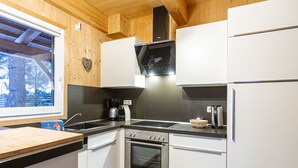A modern kitchen with white cabinets, a stainless steel oven, a black stovetop, and a window overlooking a forest.
