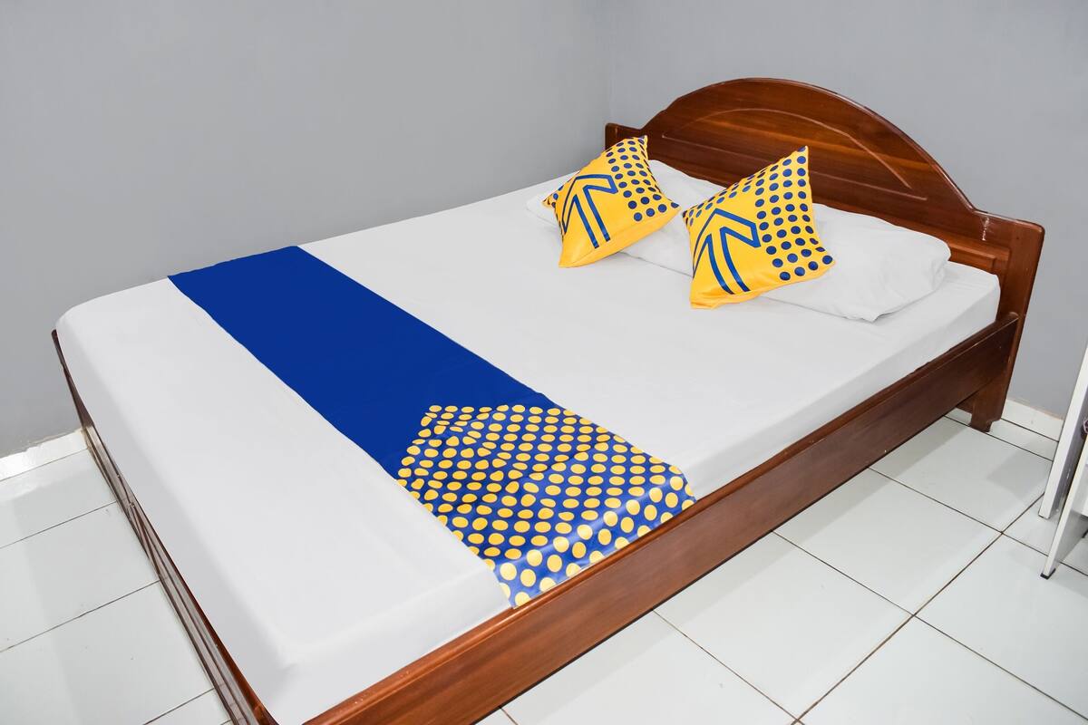 A neatly made bed with a blue and white bedspread, two yellow pillows with blue patterns, and a wooden headboard.