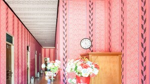 A hallway with pink wallpaper, a wooden cabinet, and a clock on the wall. - Hotel O Penginapan Widodo (Sebulu)