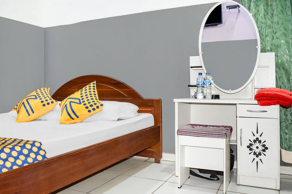 A neatly made bed with a wooden headboard, a white bedside table with a mirror, and a small white cabinet with a decorative design.
