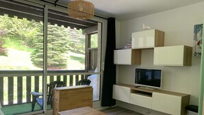 Una sala de estar moderna con un piso de vidrio corredizo a un balcón, una mesa de madera, un televisor y armarios empotrados.
