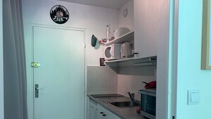Cocina compacta con gabinetes blancos, un lavamanos, un microondas y un reloj en la pared.