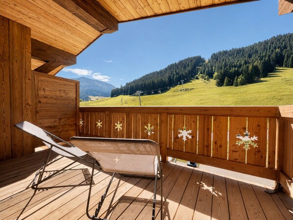 A wooden deck with two lounge chairs and a view of a mountainous landscape.