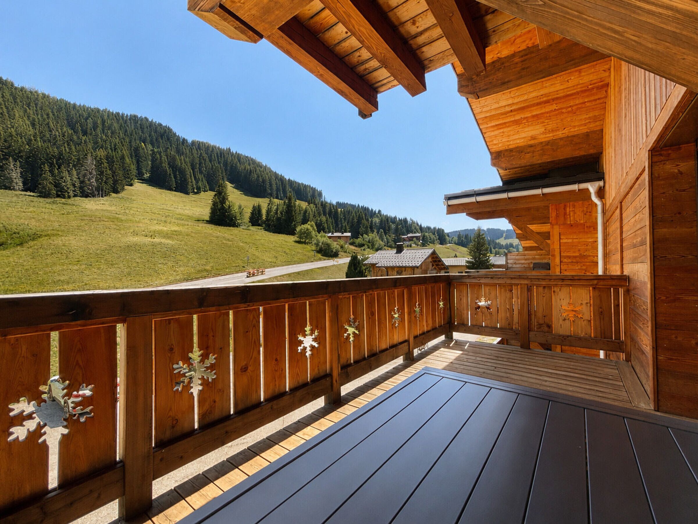 Una terraza de madera con vistas a una ladera verde y casas a lo lejos.