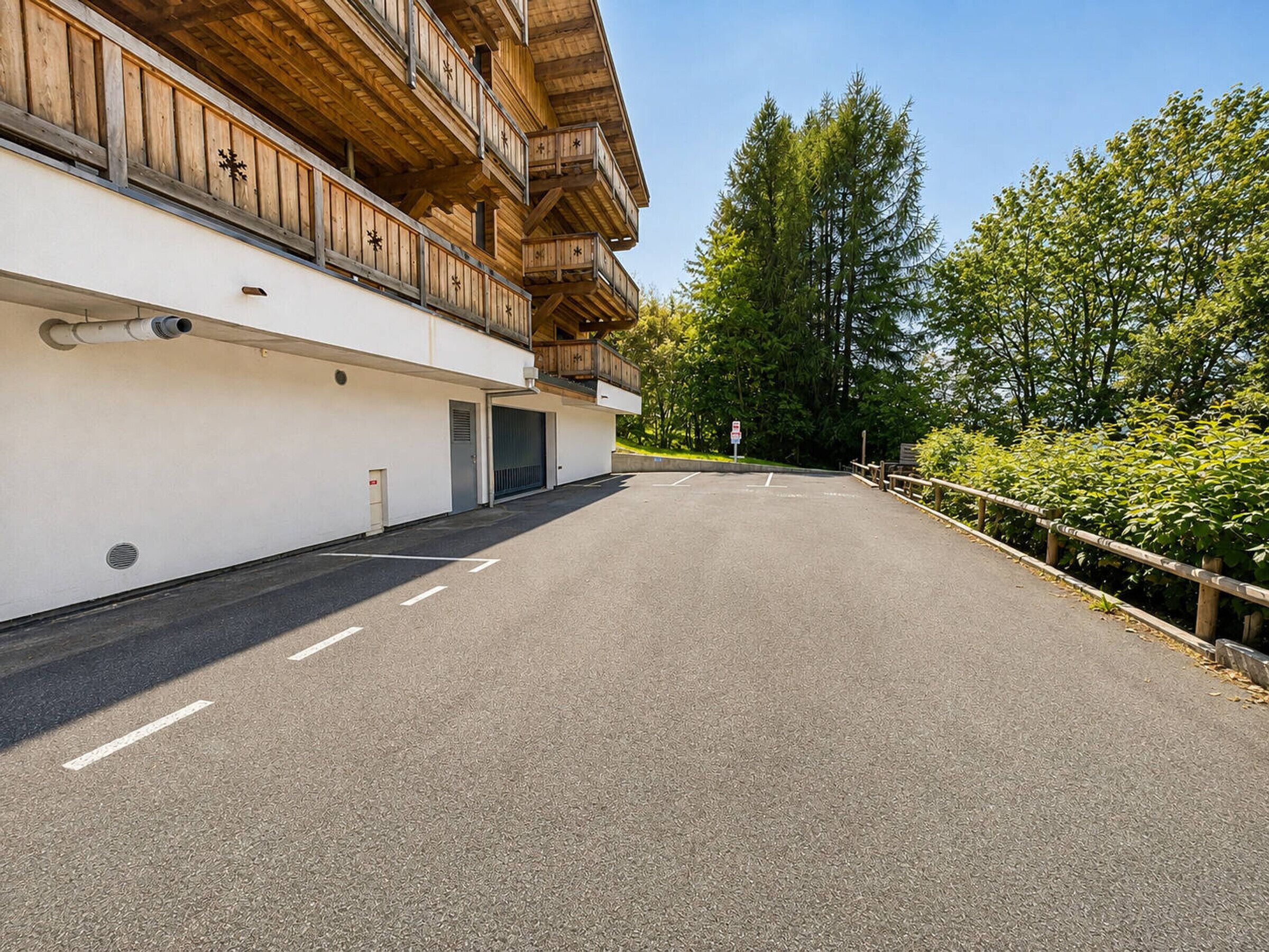 A building with a wooden balcony, a paved driveway, and a clear sky.