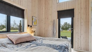 A bedroom with a large bed, a bedside lamp, a wall-mounted clock, and a window with a view of the outdoors. - Gorgeous home in Hadsund with sauna (Hadsund)
