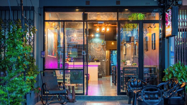 Un hostal moderno con puertas de cristal, iluminación interior y mesas al aire libre.