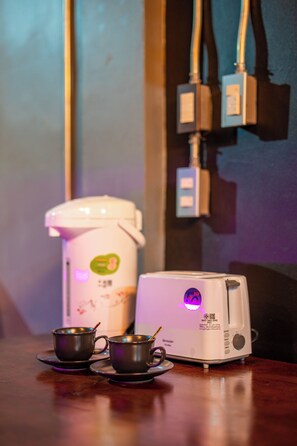 A coffee maker, two cups, and a toaster on a wooden table. - Black Panther Hostel (Phuket)