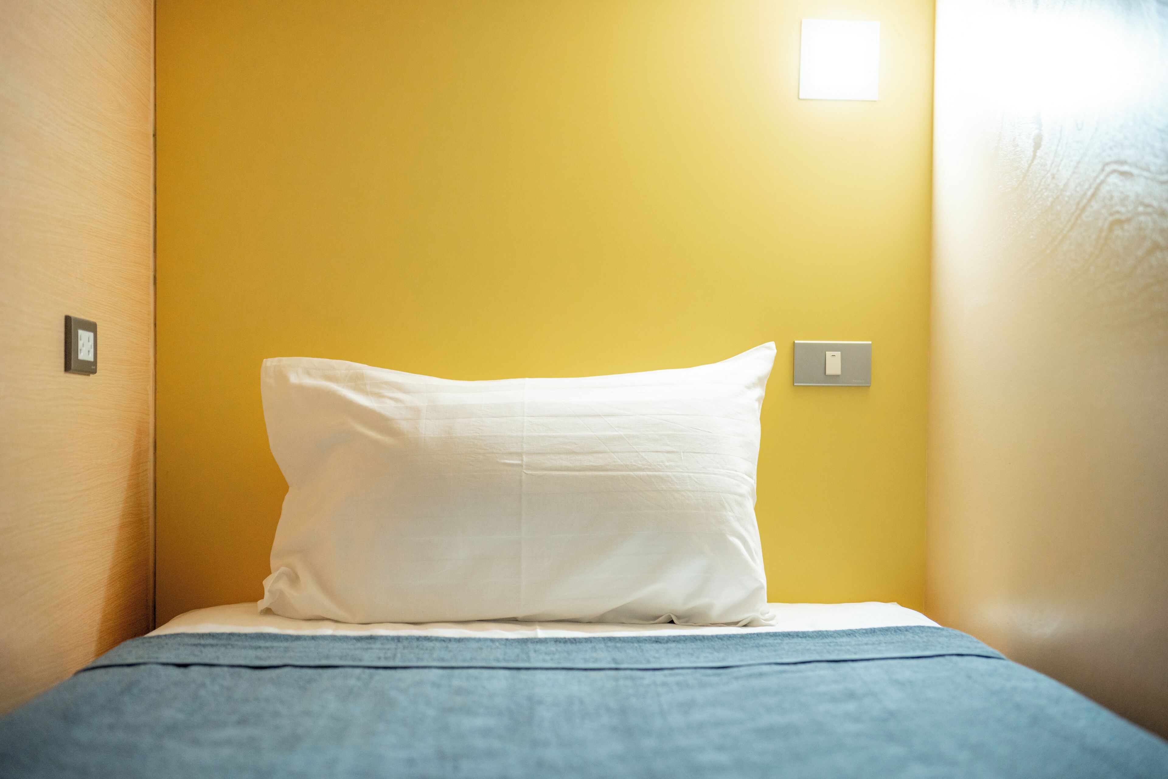 A single bed with a white pillow in a room with yellow walls.