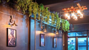 Interior de restaurante con plantas colgantes, cuadros en la pared e iluminación colgante.