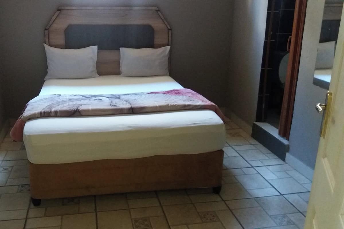 Una habitación estrecha con una cama, cabecera de madera y suelo de baldosas.