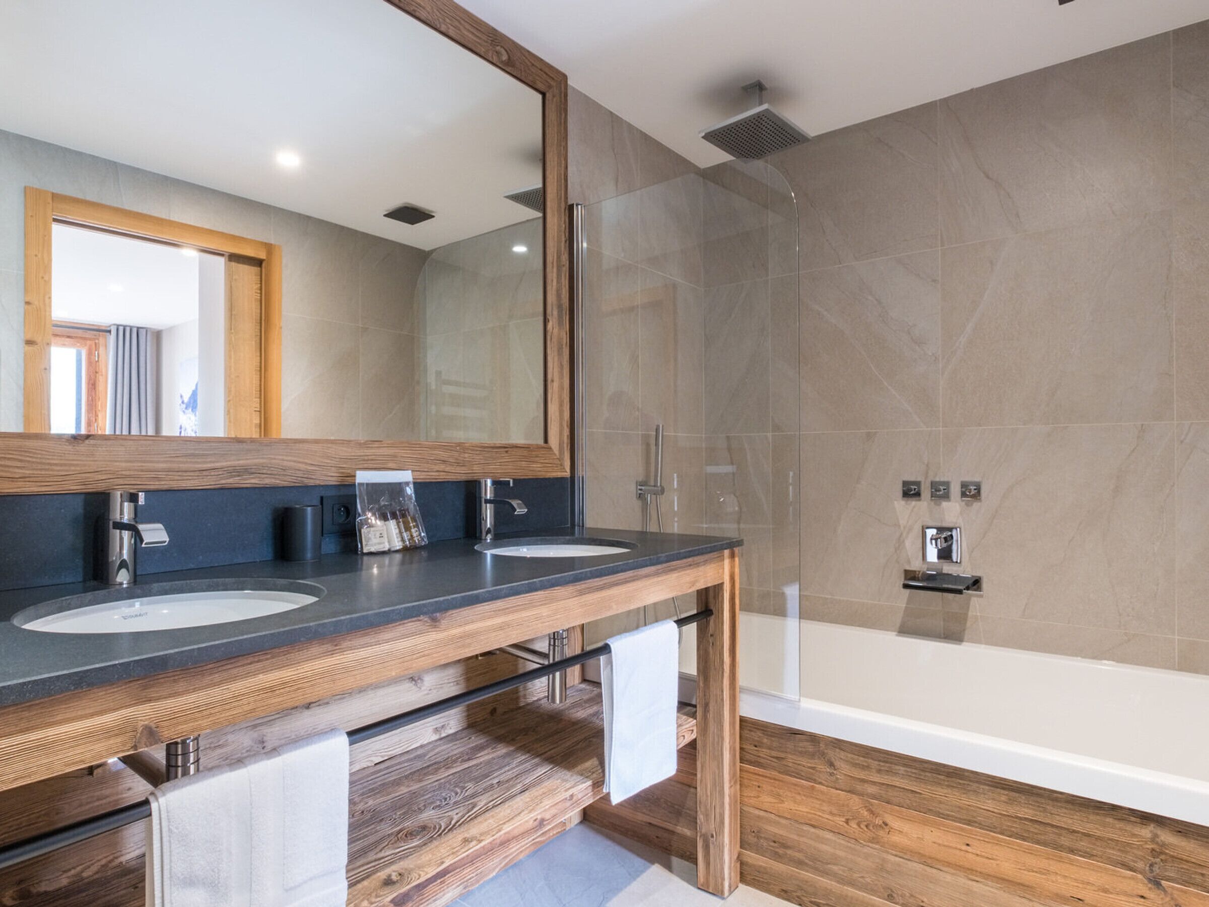 A modern bathroom with two sinks, a large mirror, and a glass-enclosed shower.