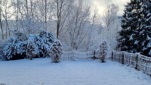 Um jardim coberto de neve, com cerca de madeira e árvores.