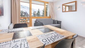 Habitació moderna amb taula de dinar de fusta, sofà gris i una finestra gran amb vista a muntanyes nevades.
