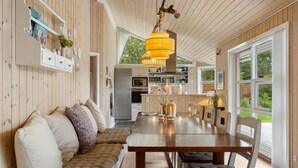 A cozy interior with a wooden bench, dining table, and chairs, a kitchen area in the background, and large windows offering a view of the outdoors. - Amazing home in Fårevejle with sauna (Fårevejle)