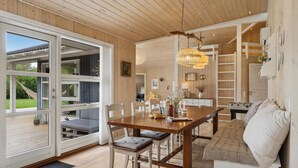 A spacious dining area with a wooden table and chairs, a chandelier, and a view through large glass doors to an outdoor deck. - Amazing home in Fårevejle with sauna (Fårevejle)