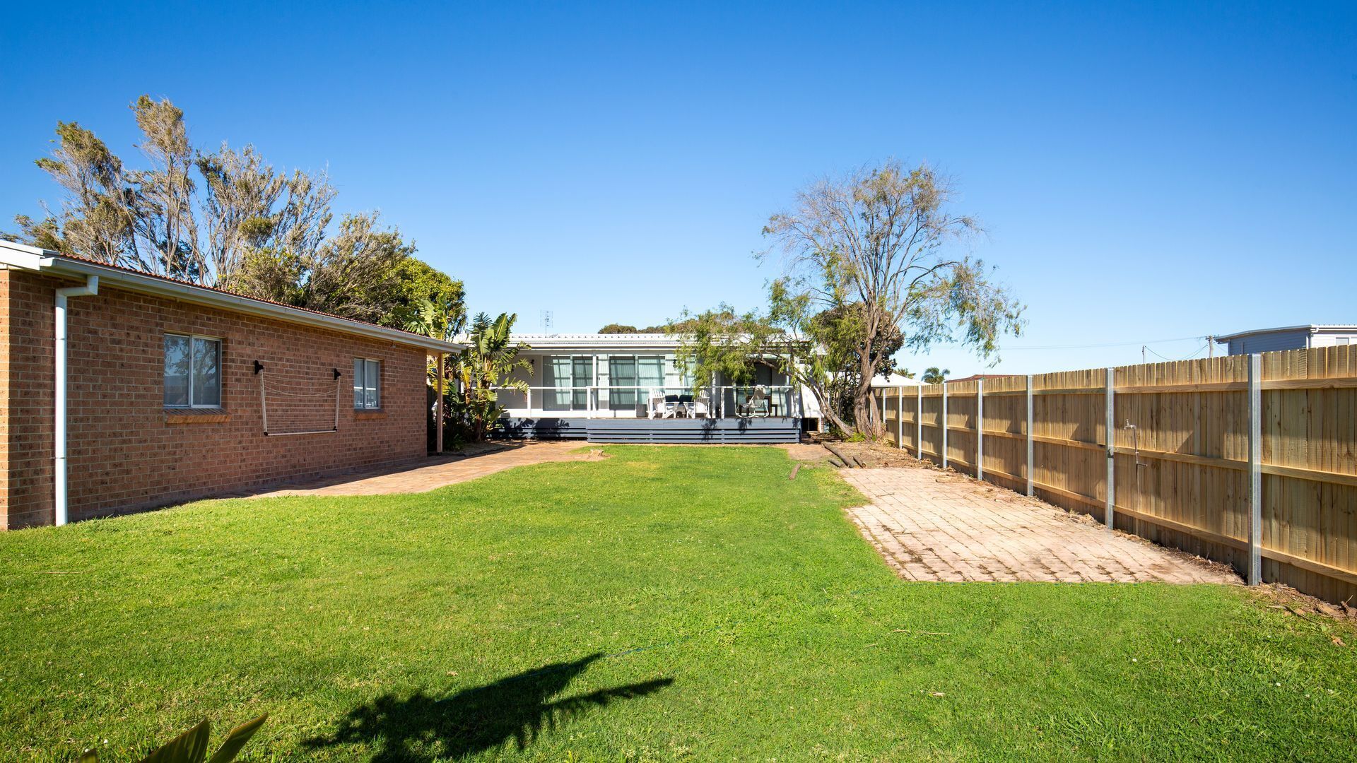 A backyard with a lawn, a brick house, a wooden fence, and a deck with outdoor furniture.
