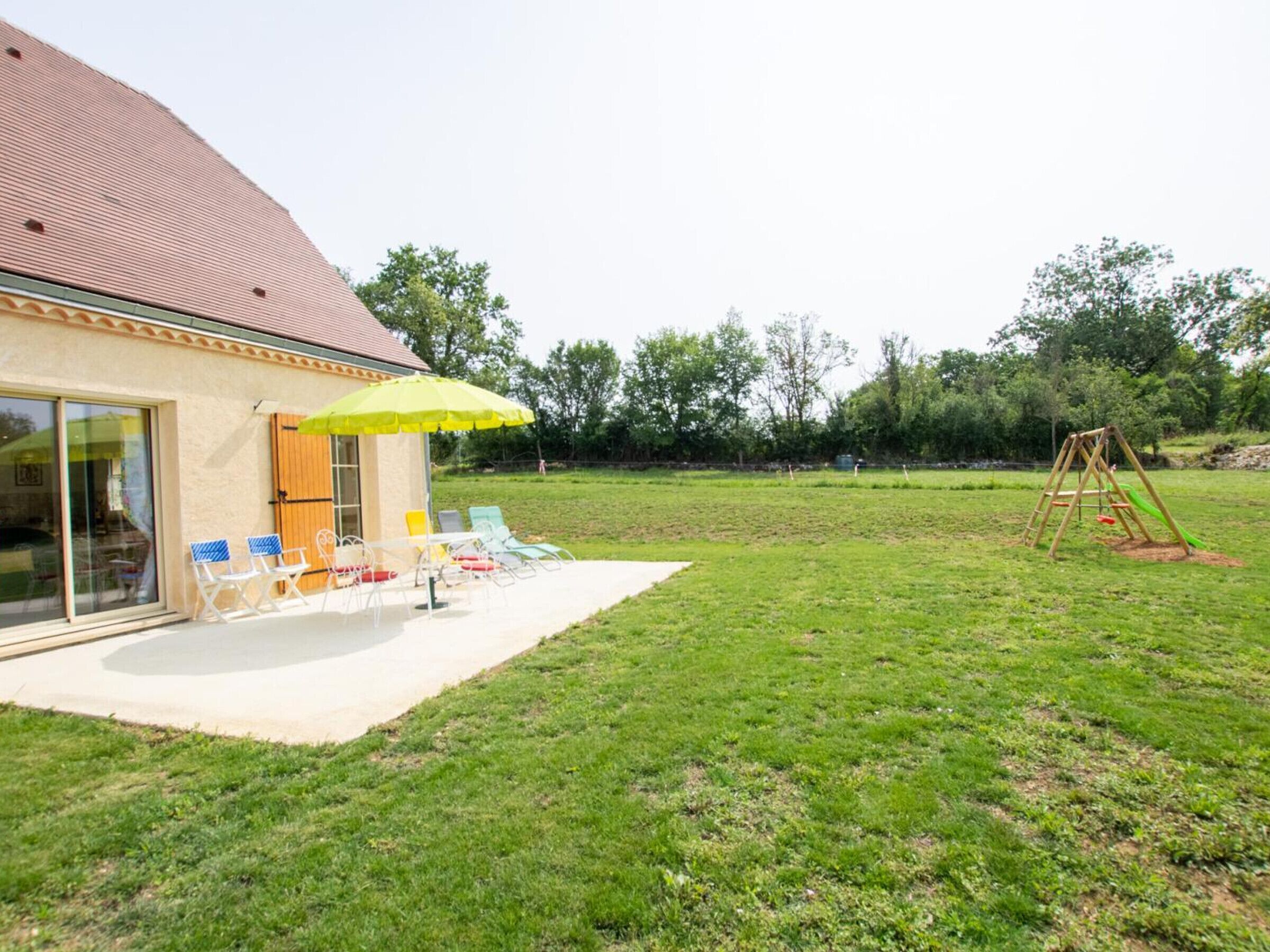 A house with a patio, outdoor seating, and a swing set.