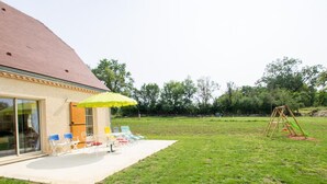 Een huis met een terras, buitenmeubels en een schommel.