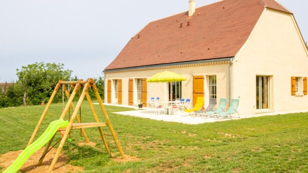 Een huis met een rood dak, een terras met tuinmeubilair en een schommel.