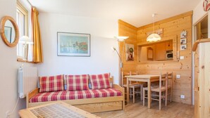 A cozy room with a wooden floor, a plaid sofa, a small wooden table, a dining table with chairs, and a kitchen area with wooden cabinets. - Cozy 2-room south, 5 pers, Avoriaz (Avoriaz)