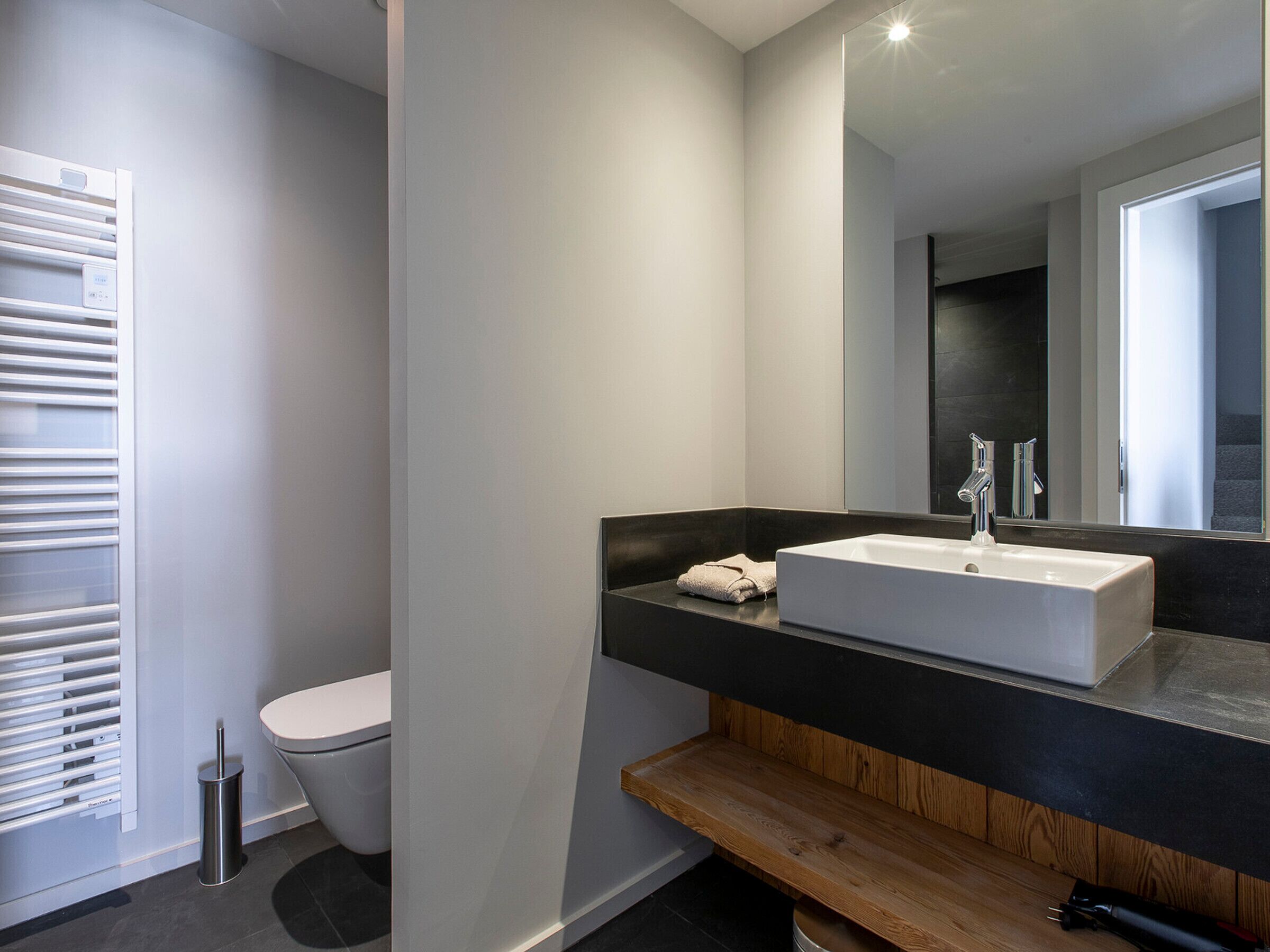 A modern bathroom with a white sink, a wooden vanity, a toilet, and a towel rack.
