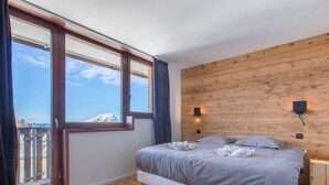 Une chambre avec une grande fenêtre, un lambris en bois, un lit avec des oreillers et une table de chevet.