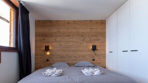 Une chambre à coucher avec une tête de lit en bois, deux lampes de chevet, un lit avec une literie grise et une armoire blanche.