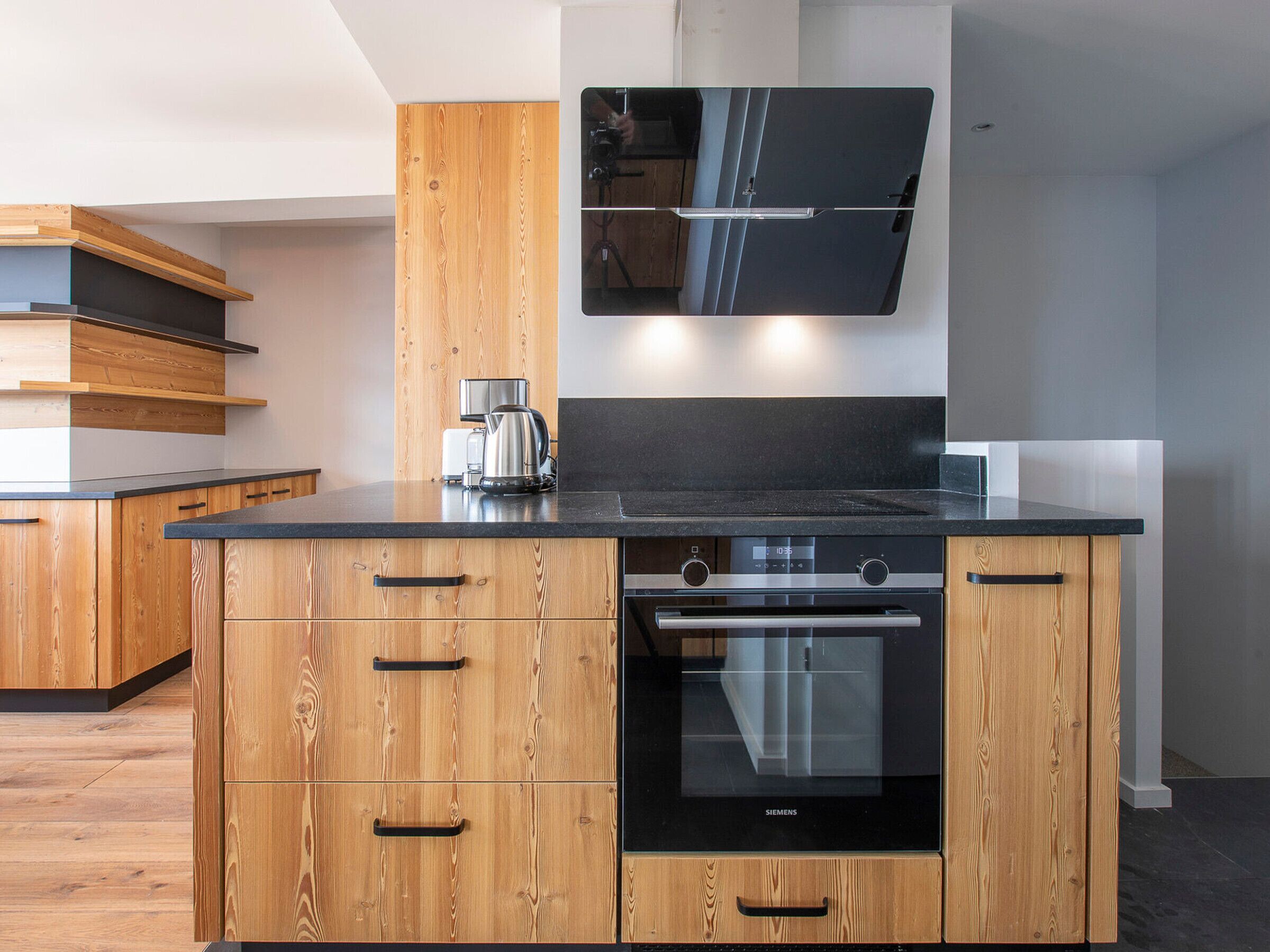 A modern kitchen with wooden cabinetry, a black countertop, a built-in oven, and a coffee maker.