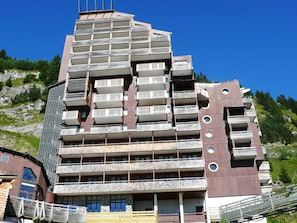 A multi-story building with balconies, a wooden facade, and a mountainous backdrop.