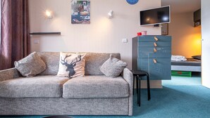 A modern living room with a grey sofa, a small table, a TV, and a dresser.