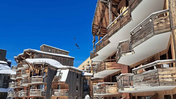 A cluster of wooden buildings with balconies, likely a ski resort accommodation.