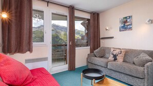 A cozy living room with a grey sofa, red cushions, a wooden coffee table, and a view of mountains through a glass door.