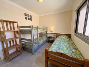 A bedroom with bunk beds, a desk, a lamp, and a window.