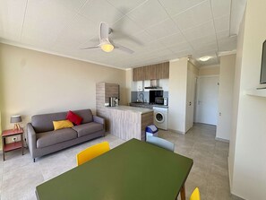 Un espacio habitable compacto con sofá, mesa de comedor, zona de cocina y ventilador de techo.