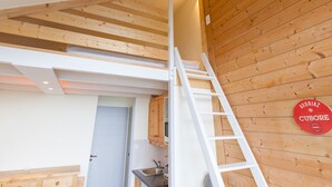 A loft-style room with exposed wooden beams, a kitchen area, and a ladder leading to a loft space.