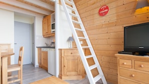A kitchen with wooden cabinets, a white countertop, a microwave, and a stove. There is a white ladder leaning against the wall and a television on a wooden stand.