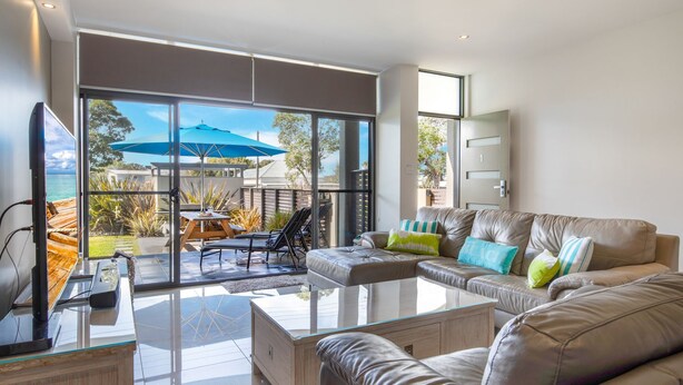 A modern living room with a glass coffee table, leather sofa, and a view of the outdoors. - Serenity Shores by Book Jervis Bay (Huskisson)