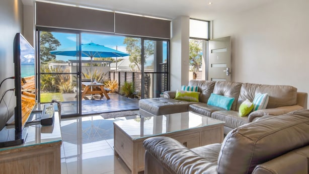 A modern living room with a glass coffee table, leather sofa, and a view of the outdoors through large windows. - Interlude Apartment by Book Jervis Bay (Huskisson)