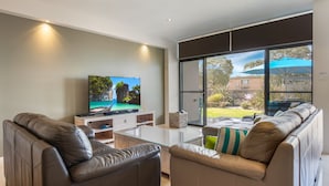 A modern living room with leather sofas, a flat-screen TV, and a glass coffee table. - Interlude Apartment by Book Jervis Bay (Huskisson)