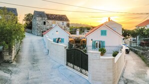 Una calle estrecha con casas de piedra, un portón y el atardecer al fondo.