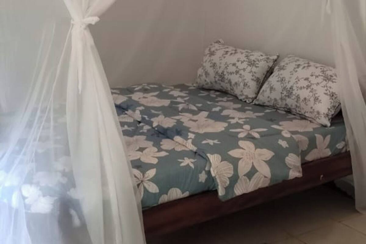 A room with a bed under a white canopy, a floral bedspread, and a red mat on the floor.